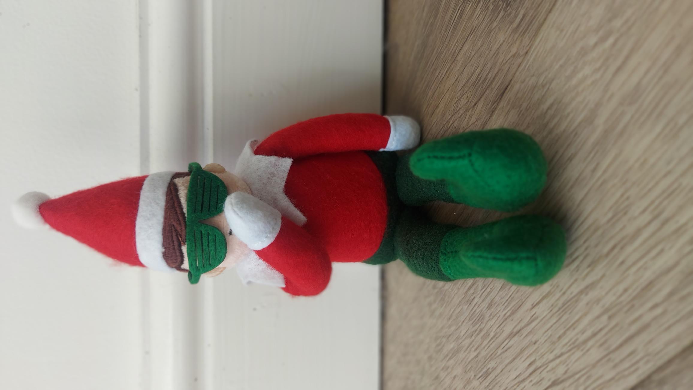 Official Cheeky Elves Jingles Doll against a wall